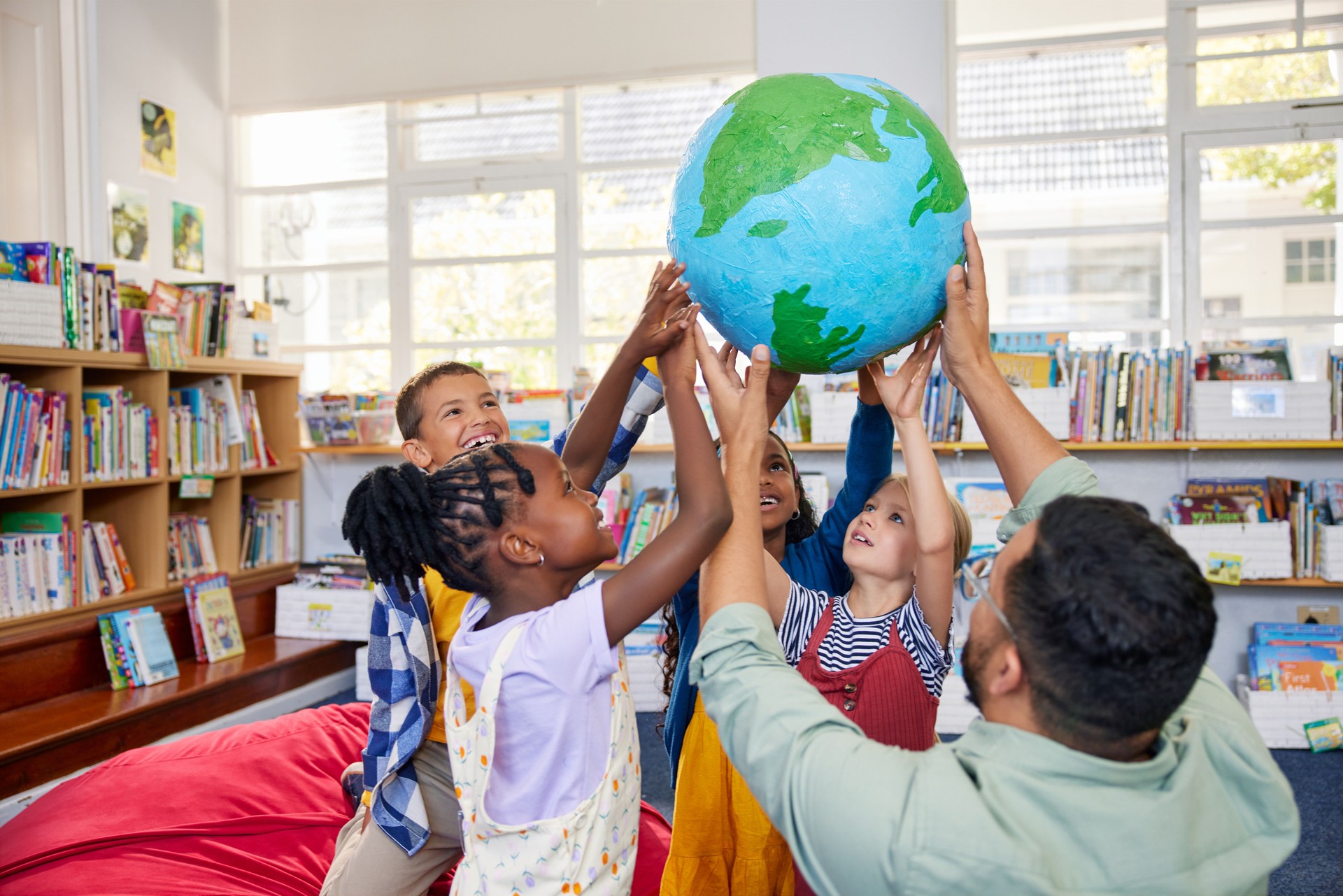 School children with teacher holding earth model in a library